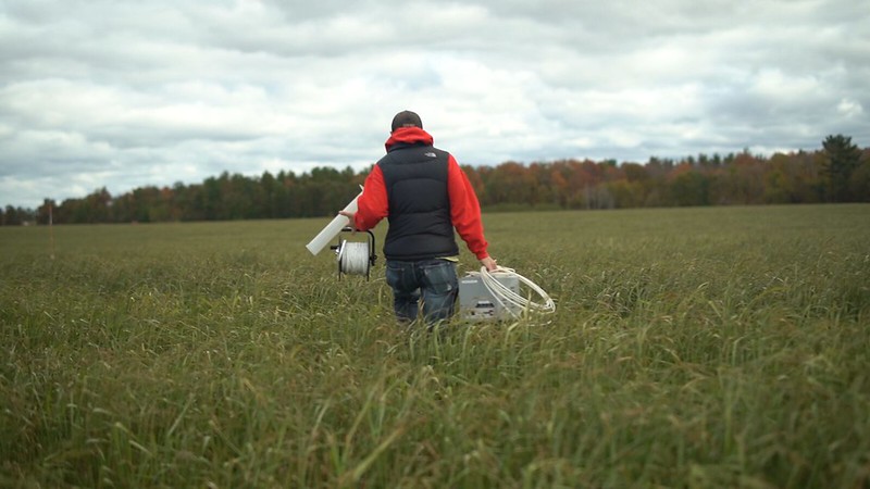 Person carrying equipment and walking through green field.