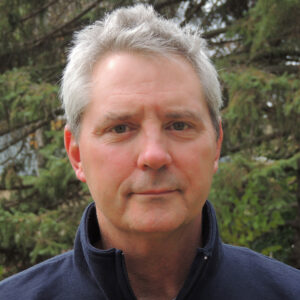 Closeup of person standing in front of evergreen trees. 